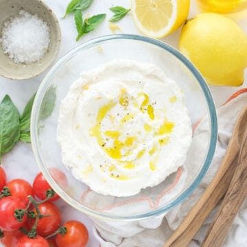 Top view of a glass bowl full of ricotta, tomatoes and lemons in the background.