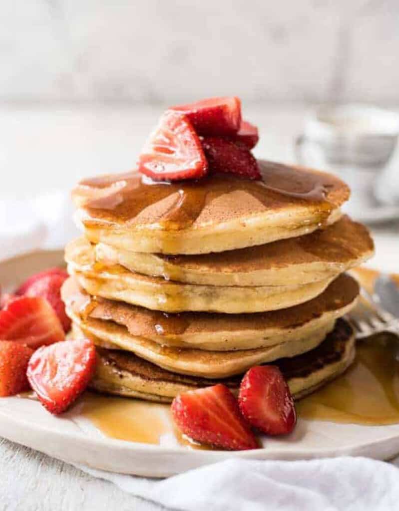 A pile of soft ricotta pancakes with maple syrup and strawberries.
