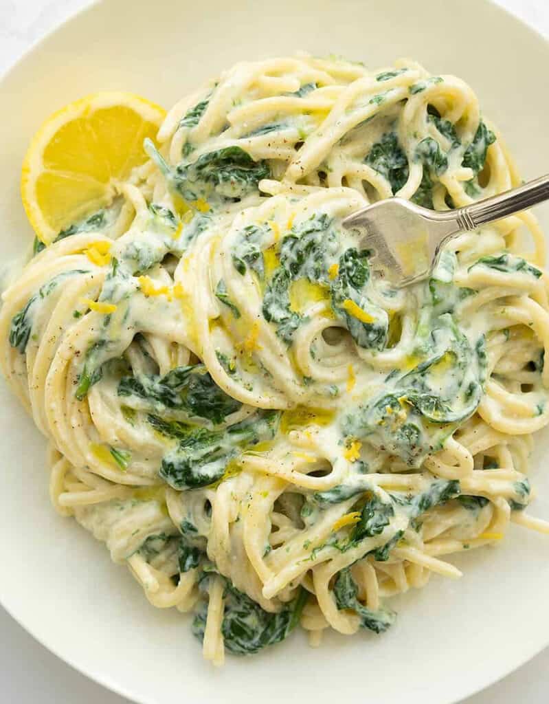 A white plate full of spaghetti with creamy ricotta sauce, spinach and lemon zest.