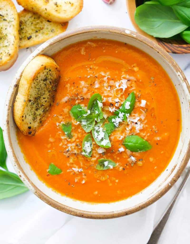 Top view of a bowl full or creamy tomato soup with potatoes and fresh basil leaves.