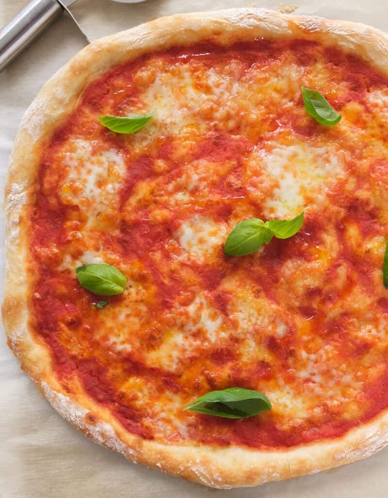 Top view of a large crusty easy no-knead pizza topped with tomato sauce, mozzarella and fresh basil leaves.