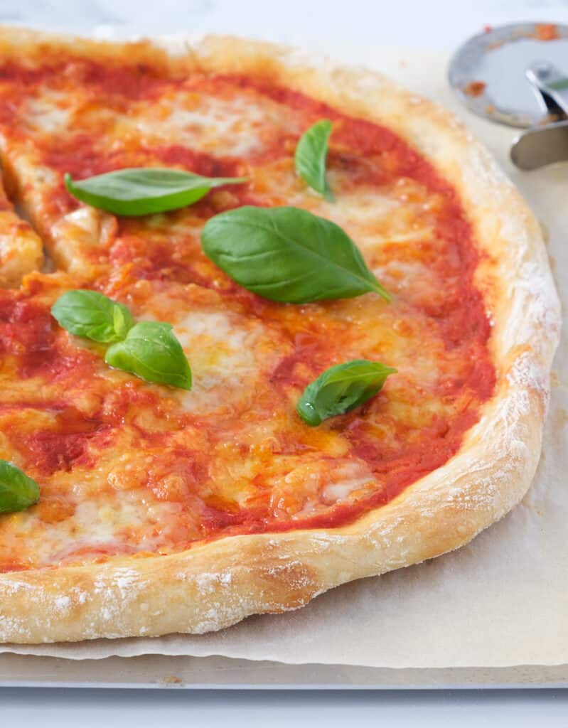 Close-up of a large pizza with fresh basil leaves made with easy no-knead pizza dough.
