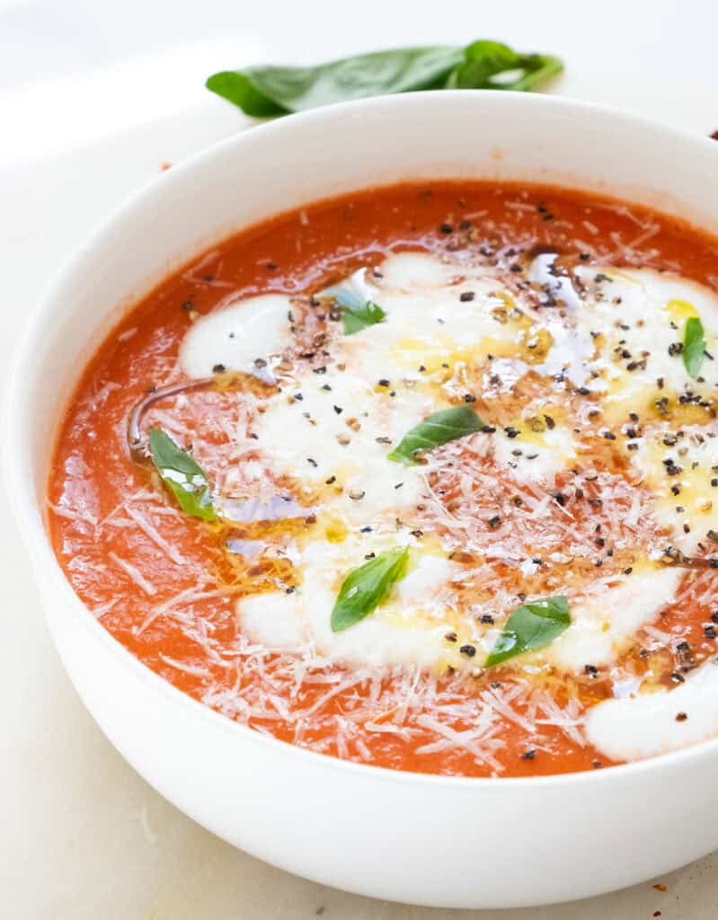 A white bowl full of a simple homemade tomato soup topped with cream fresh and basil.