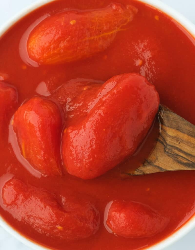 Top view of a white bowl full of canned whole tomatoes and their juice.