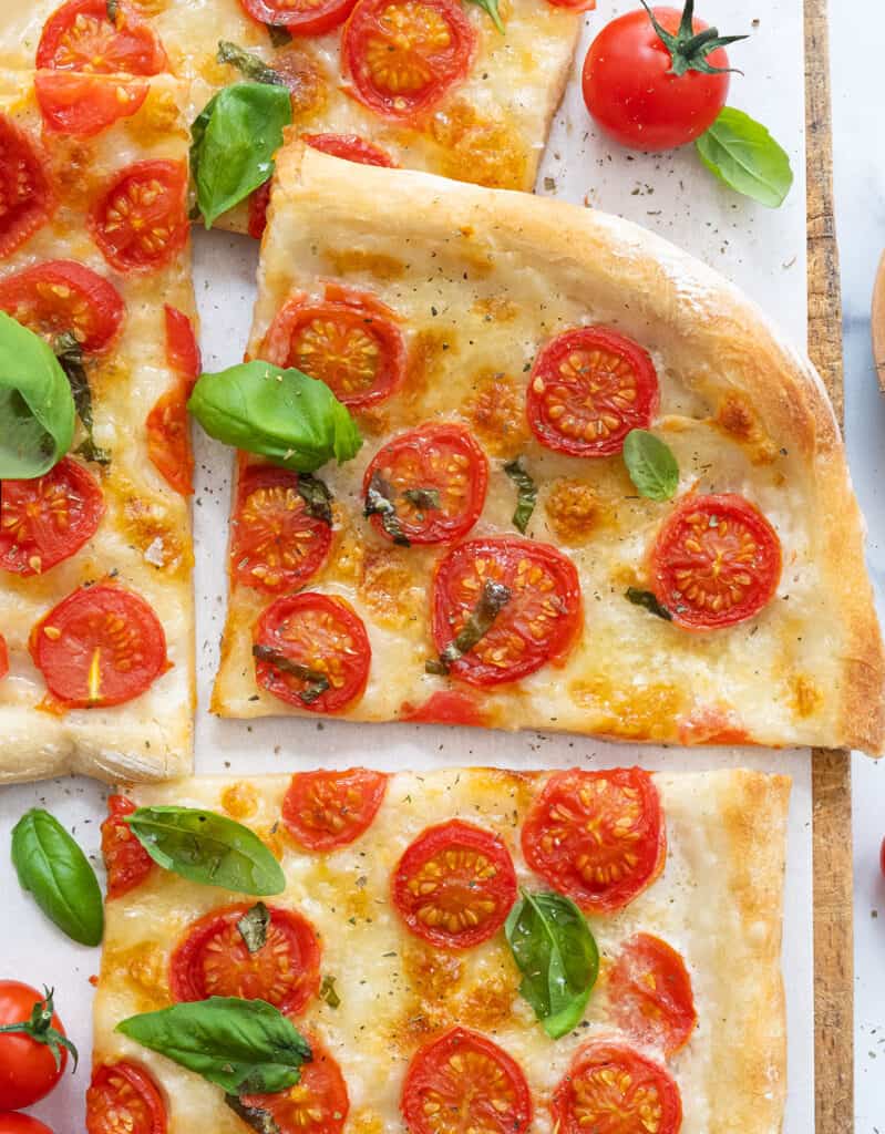 Top view of a fresh tomato pizza with fresh basil leaves cut into slices.