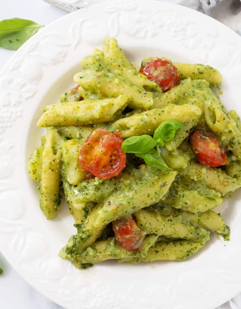 Top view of a white plate full of penne with pesto and cherry tomatoes.