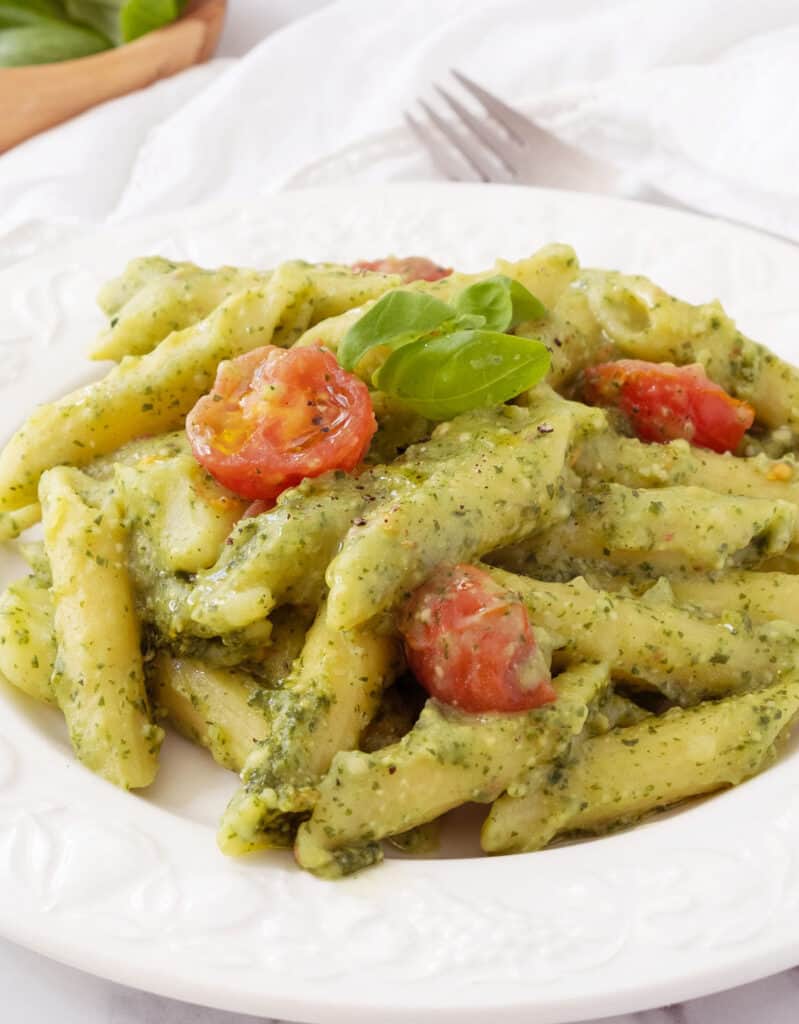 A white plate full of penne with pesto and cherry tomatoes.