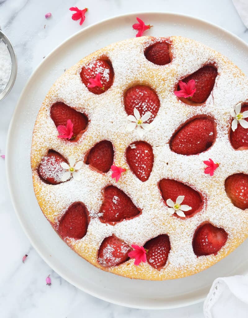 Top view of a round ricotta cake with strawberries over a white background.