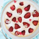 Top view of a round strawberry ricotta cake over a tourquois background.