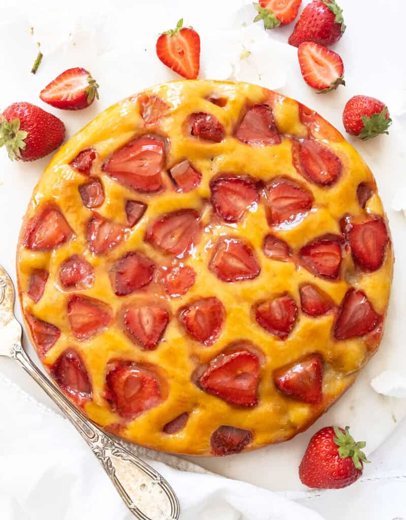 Top view of a round strawberry ricotta cake over a white background.