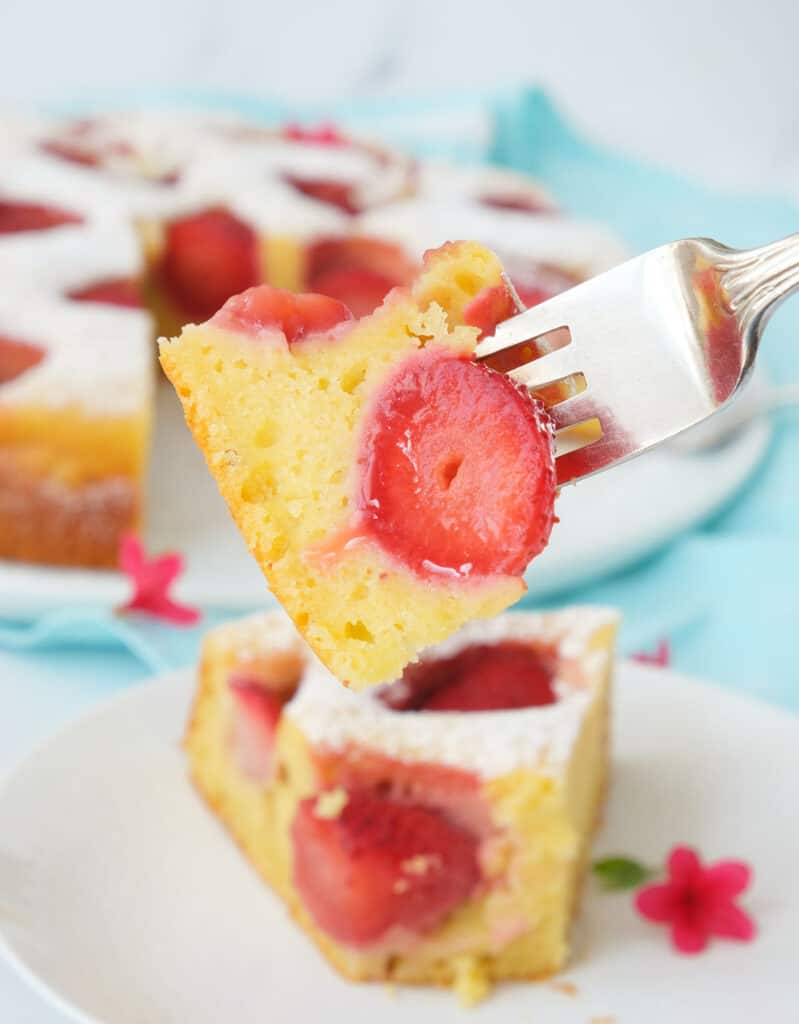 A fork lifting a piece of strawberry ricotta cake showing the juicy strawberries inside.