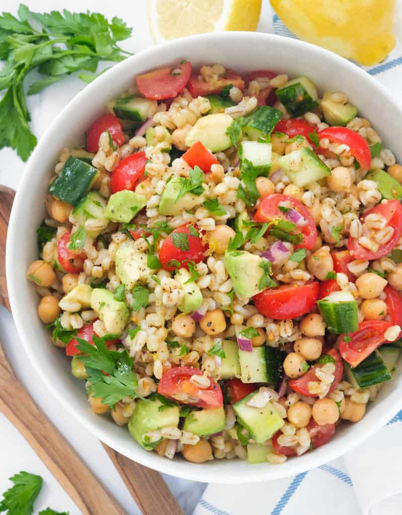 Top view of a white salad bowl full of barley salad with cherry tomatoes, diced cucumber and herbs.