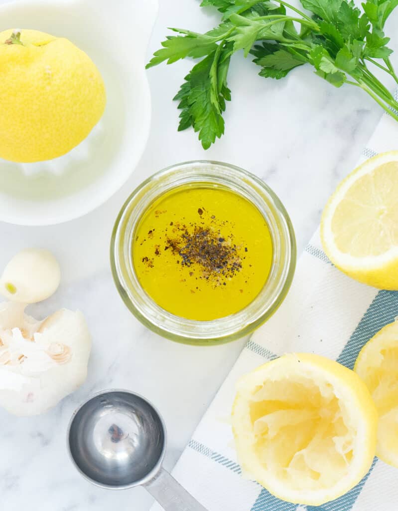 Top view of a glass jar full of lemon garlic dressing, lemons and parsley in the background.