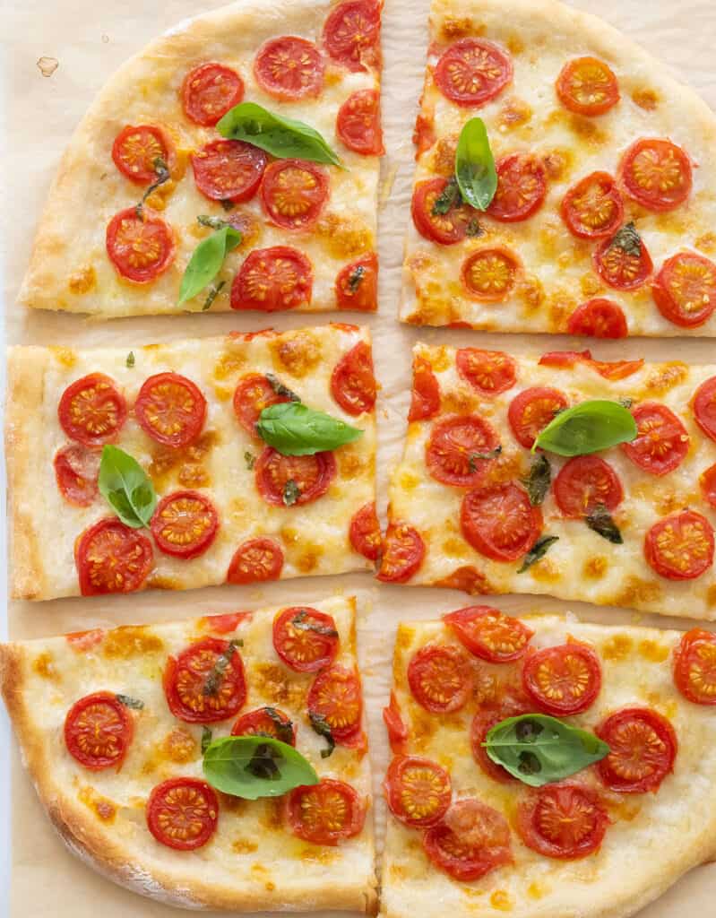 Top view of a whole fresh tomato pizza cut into slices and garnished with fresh basil leaves.