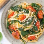 Top view of a grey plate with pasta with tomatoes and spinach.