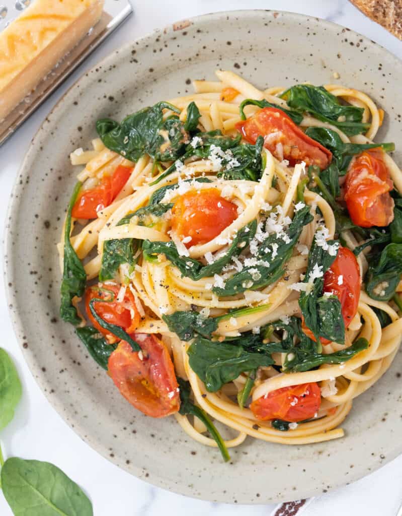 Top view of a grey plate full of pasta with tomatoes and spinach.