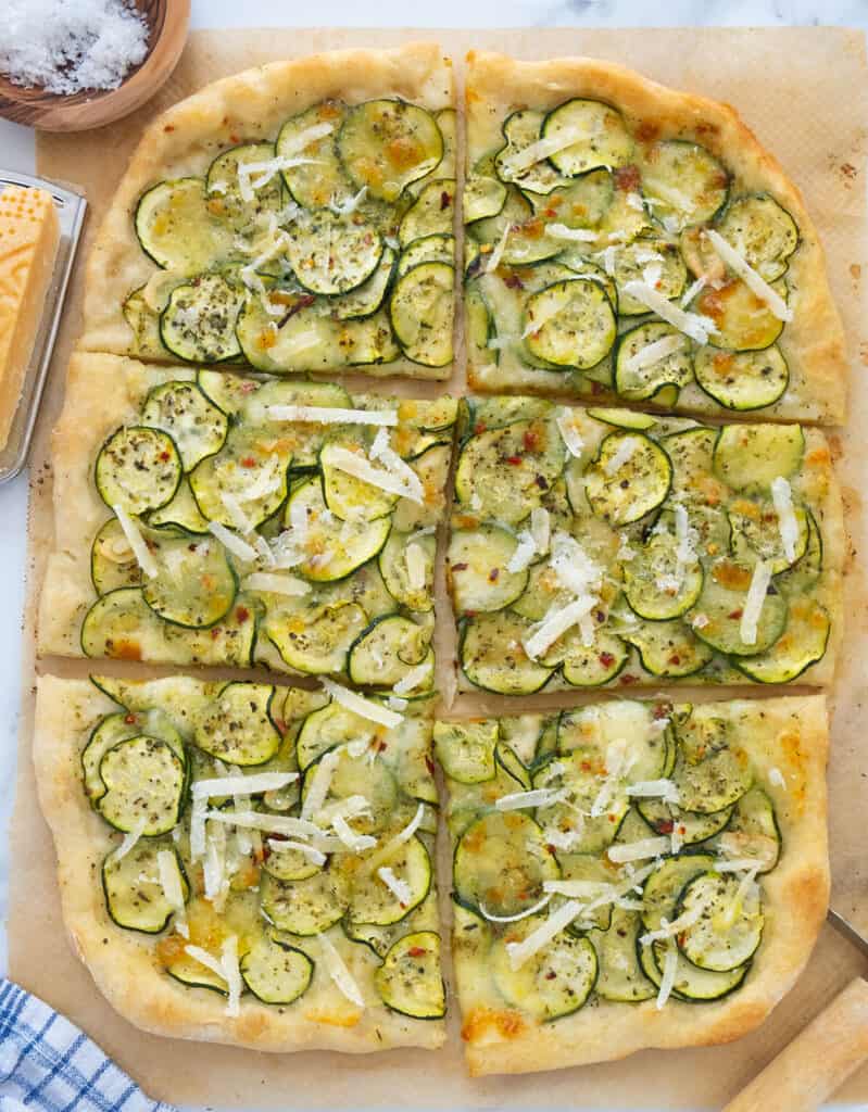 Top view of a large pizza with zucchini cut into six slices and garnished with shaved parmesan.