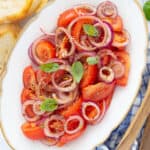 Top view of a white serving plate full of onion and tomato salad.