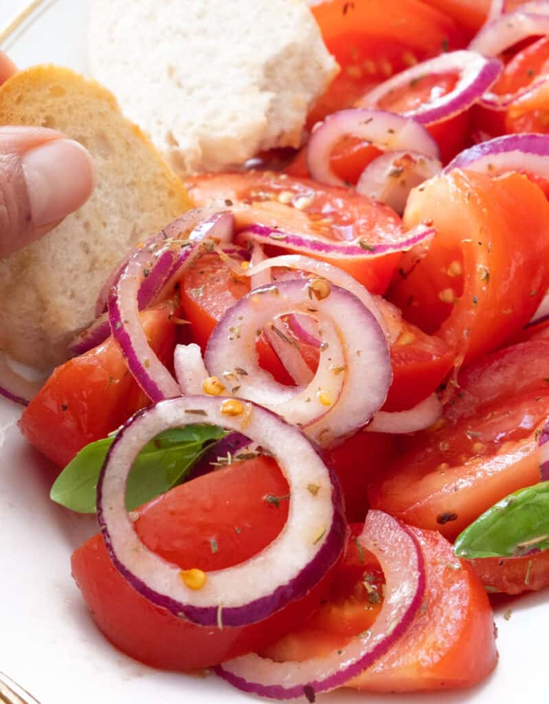 A hand digging a slice of crusty bread into some tomato and onion salad.