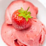 Close-up of a white bowl full of frozen strawberry yogurt topped with a fresh strawberry.