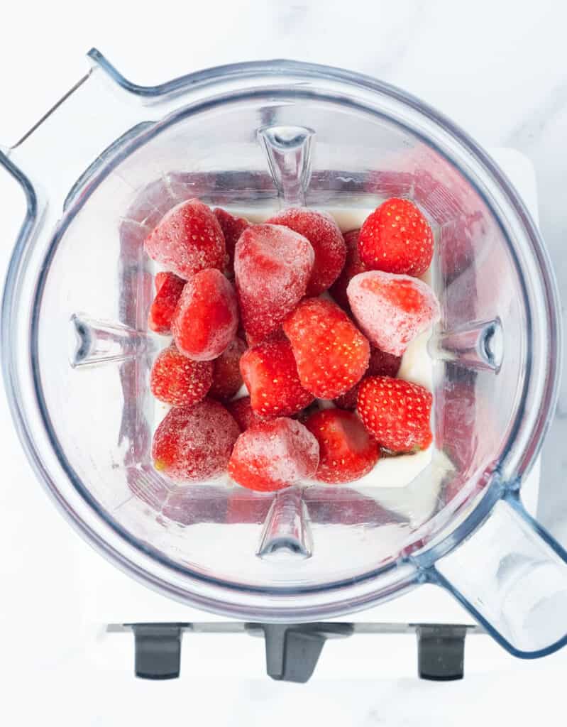 Top view of a Vitamix blender full of frozen strawberries and yogurt.