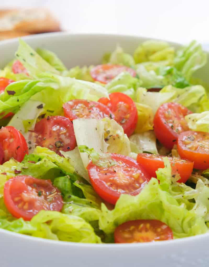 Close-up of a white bowl full of lettuce salad with cherry tomatoes.