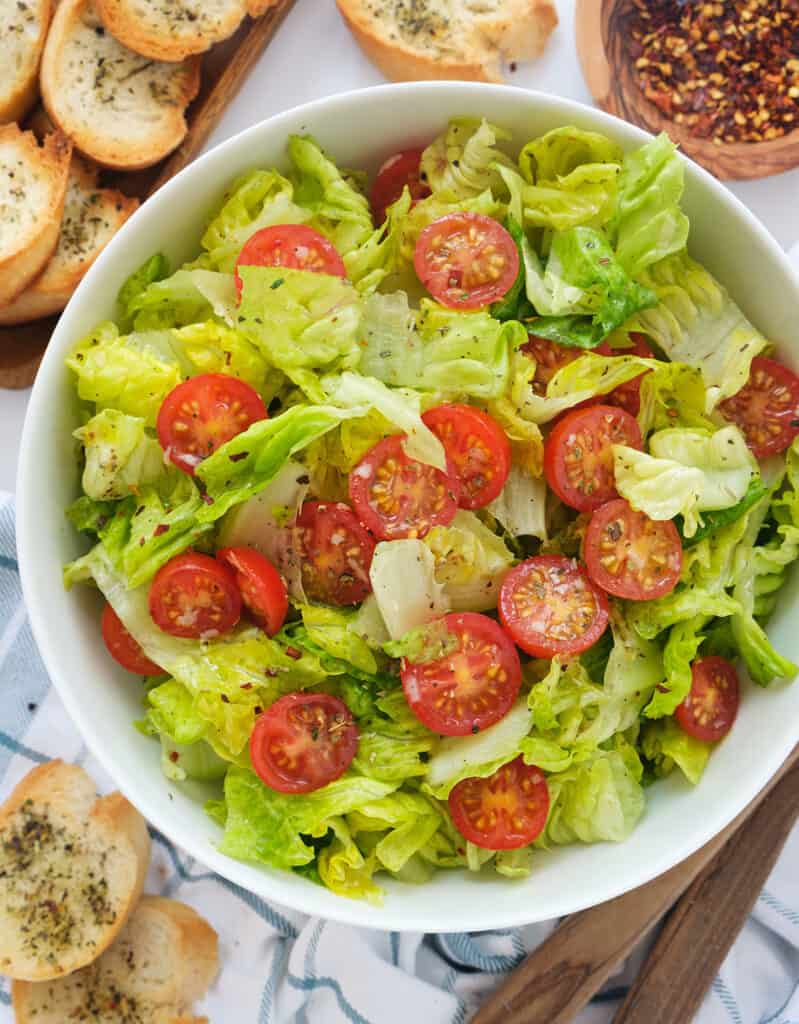 Top view of a white bowl full of lettuce salad and cherry tomatoes.