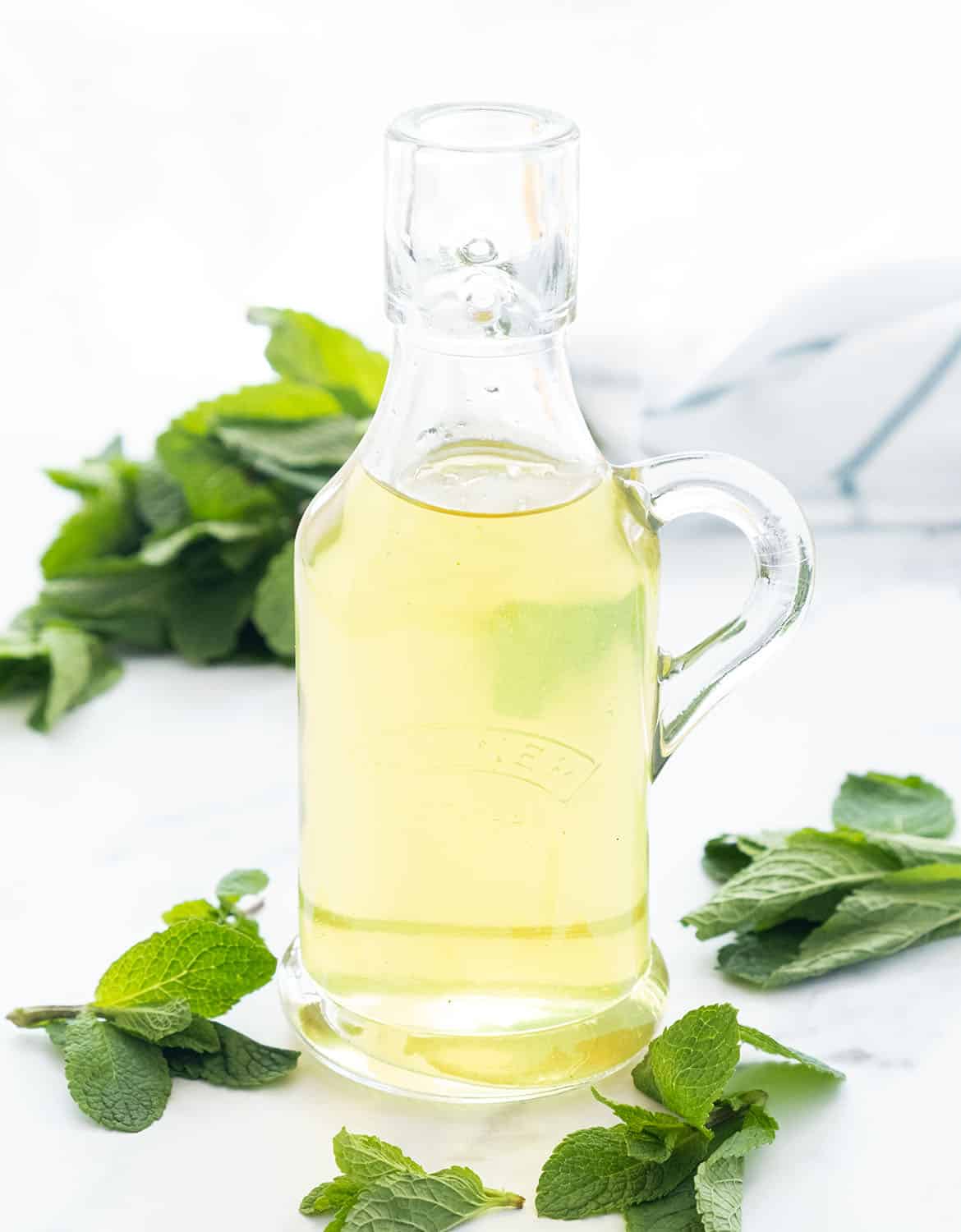 A small glass bottle full of mint syrup and mint leaves over a white background.