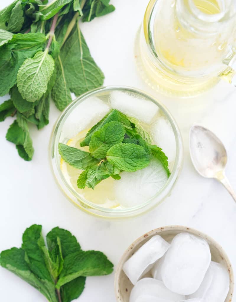 Top view of a glass full of water, ice, mint leaves and mint syrup over a white background.