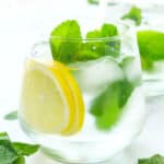 A glass full of mint water with slices of lemon and mint leaves.