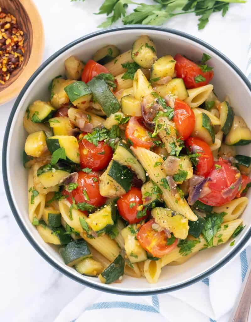 Top view of a bowl full of pasta with tomatoes and zucchini garnished with chopped parsley.