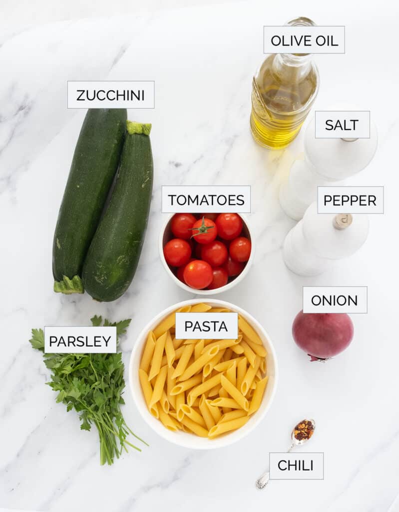 The ingredients to make this pasta with zucchini are arranged over a white background.