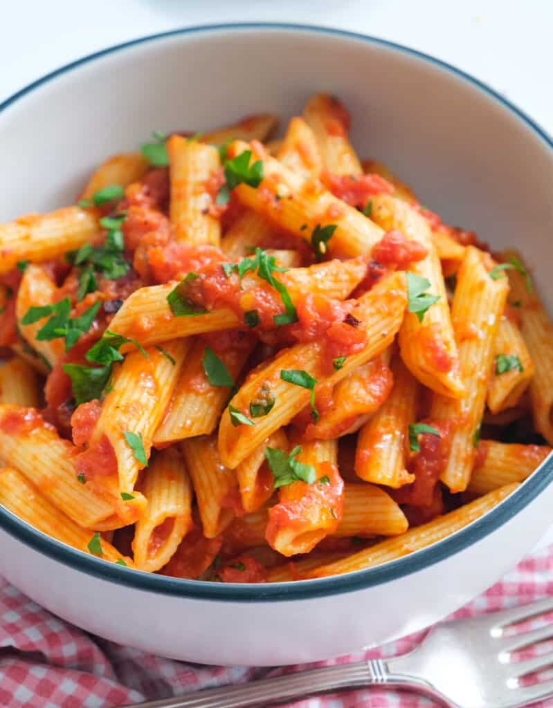 Close-up of a bowl full of penne arrabbiata with fresh parsley.