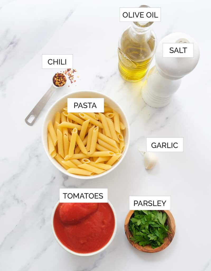 The ingredients to make penne arrabbiata are arranged over a white background.