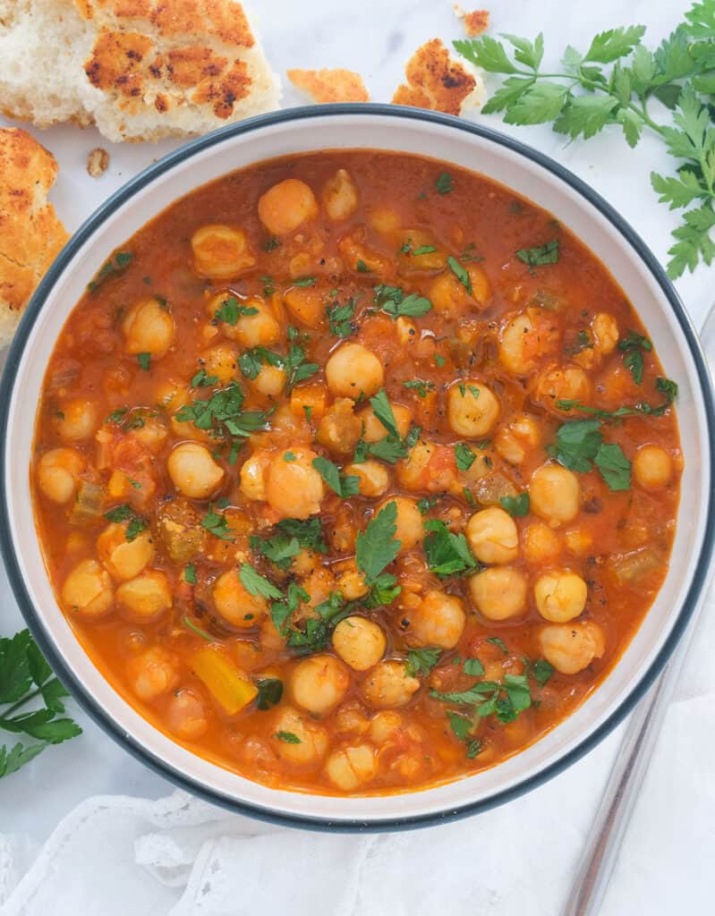 Top view of a white bowl full of chickpea stew served with crusty bread.