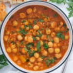 Top view of a white bowl full of chickpea stew served with crusty bread.