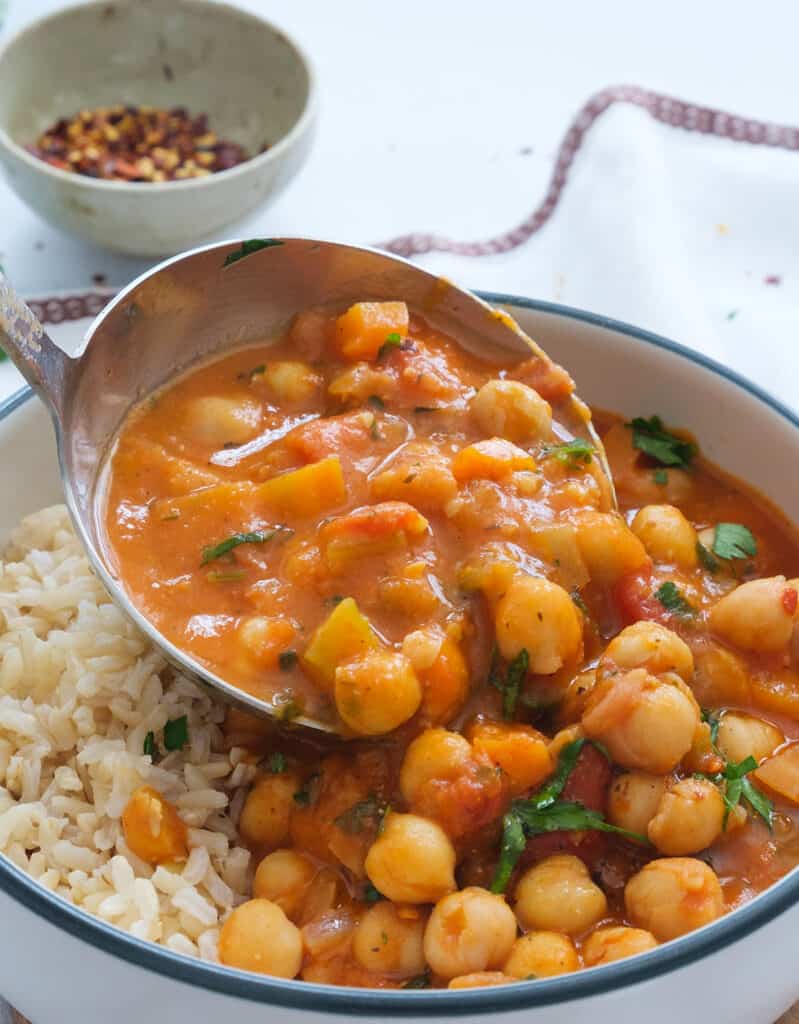 Close-up of a ladle full of chickpea stew and rich tomato sauce.