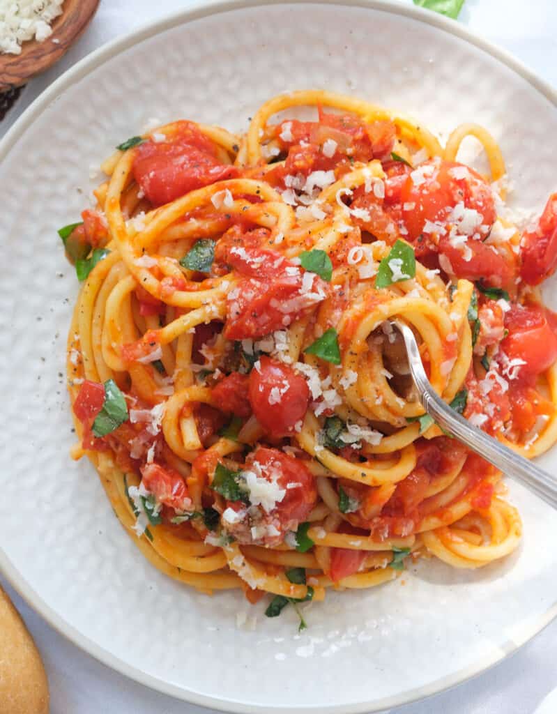 Top view of a white plate full of pasta napoletana with fresh basil.