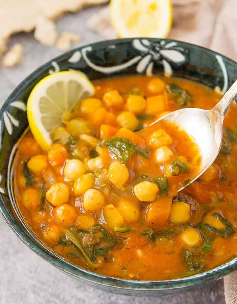 Close-up of a spoon full of chickpea soup made with spices and canned tomatoes.