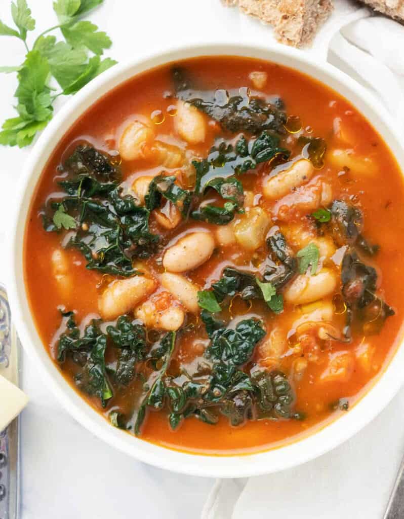 Top view of a white bowl full of white bean and kale soup made with canned tomatoes.