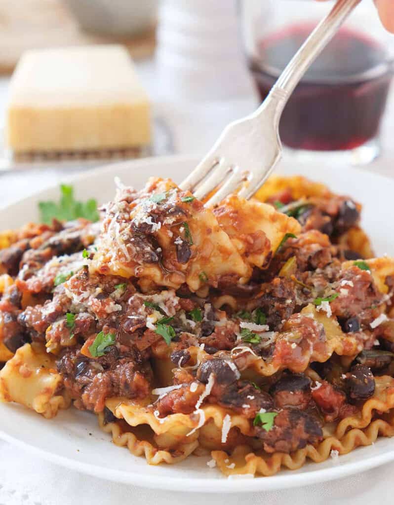 Close-up of a white plate full of pasta with black beans and tomato sauce.