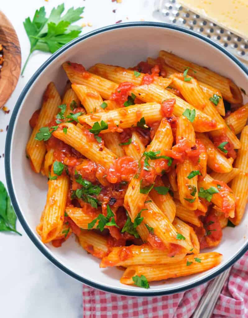 Top view of a white bowl full of penne arrabbiata made with canned tomatoes and chili flakes.