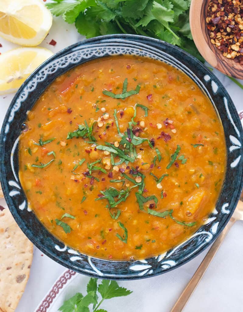 Top view of a dark blue bowl full of spicy tomato lentil soup.