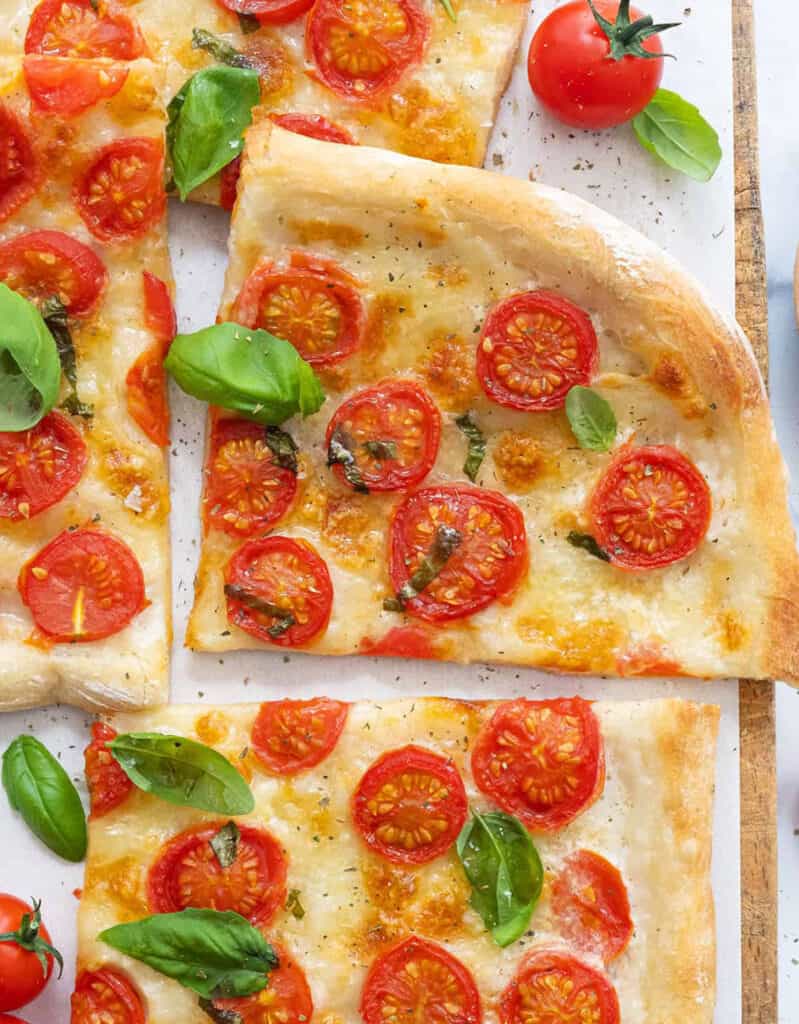 Close up of slices of fresh tomatoes pizza with fresh basil leaves.