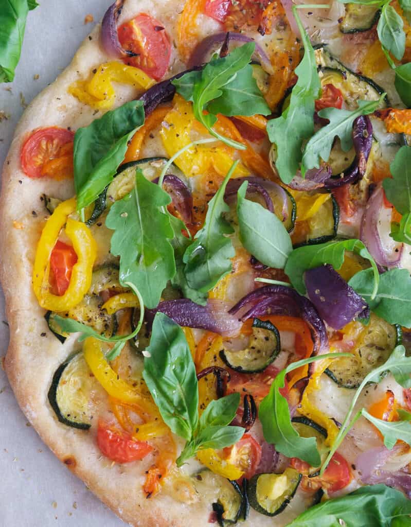 Close-up of a pizza with vegetarian topping made with roasted veggies and arugula.