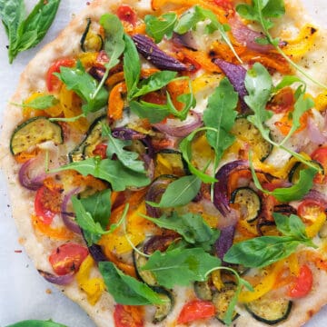 Top view of a veggie pizza with roasted vegetable, arugula and fresh basil.