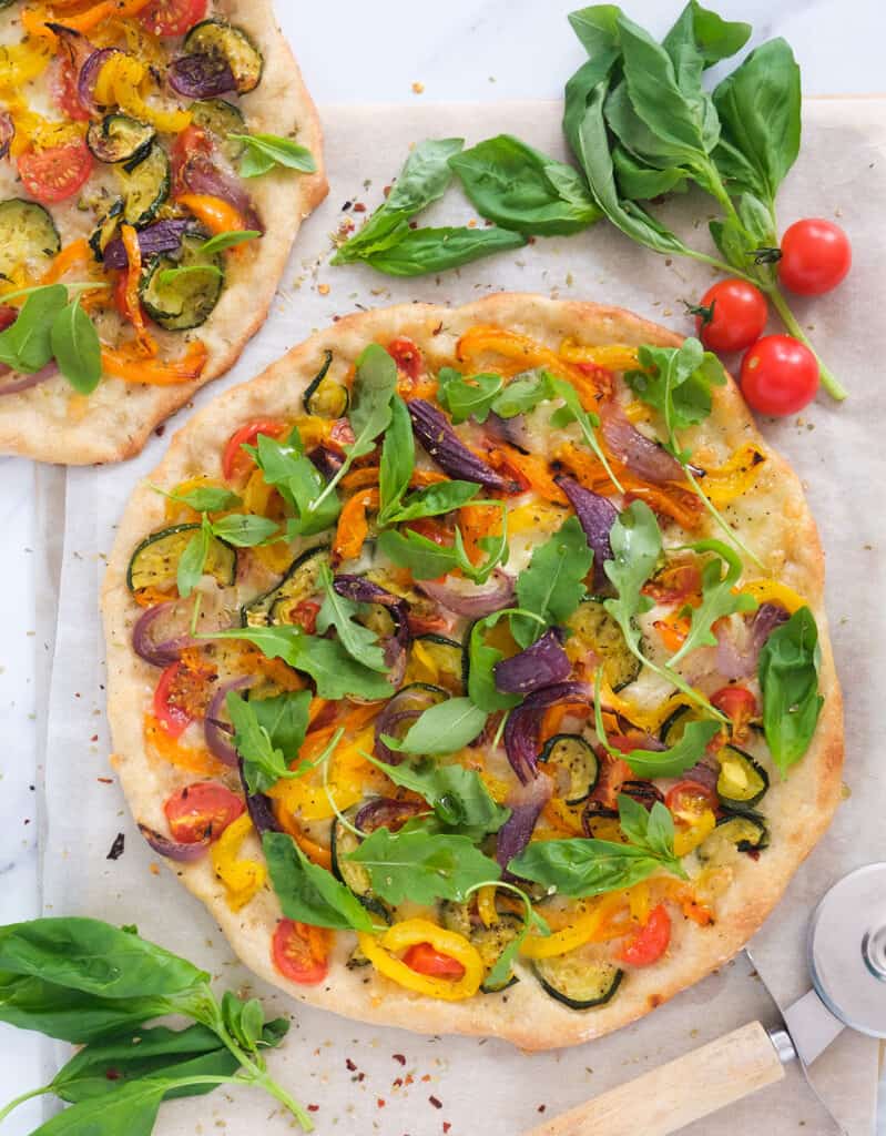 Top view of a round vegetarian pizza over a white background. Cherry tomatoes and basil leaves in the background.