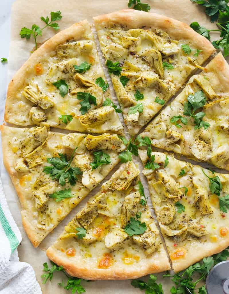 Top view of a round artichoke pizza with mozzarella cheese and fresh parsley leaves.