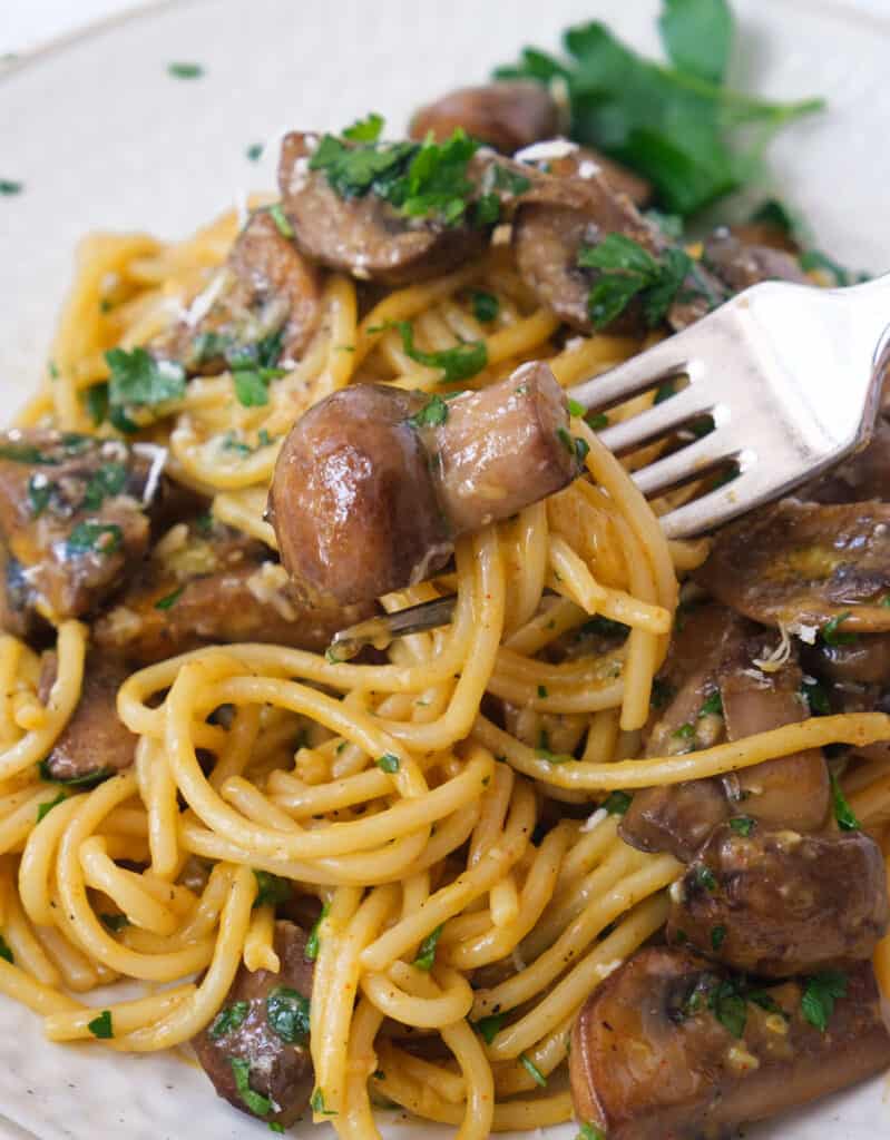 A  fork with spaghetti carbonara with mushrooms garnished with fresh parsley.