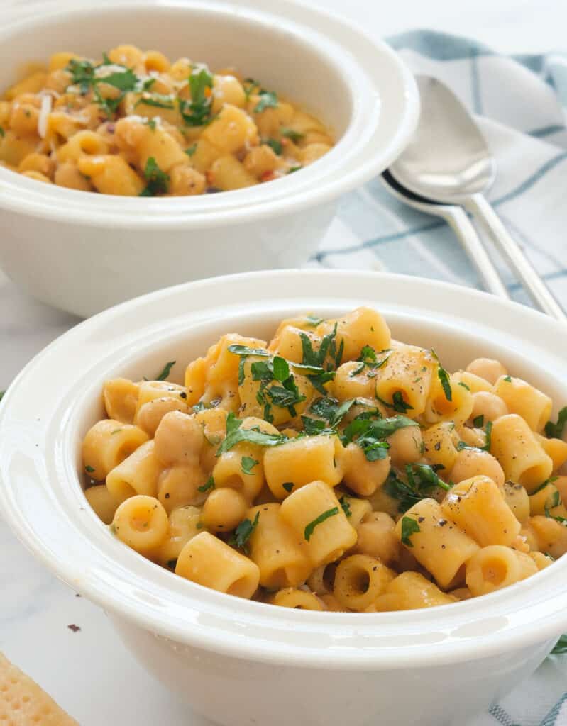 Two white bowl full of Italian pasta e ceci garnished with chopped parsleu.